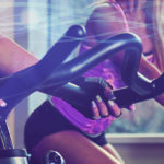 Four people in purple tops on exercise bikes in a spinning class