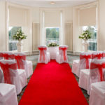 The Senate Room at mercure gloucester bowden hall hotel with chairs dressed in red sashes ready for a wedding ceremony