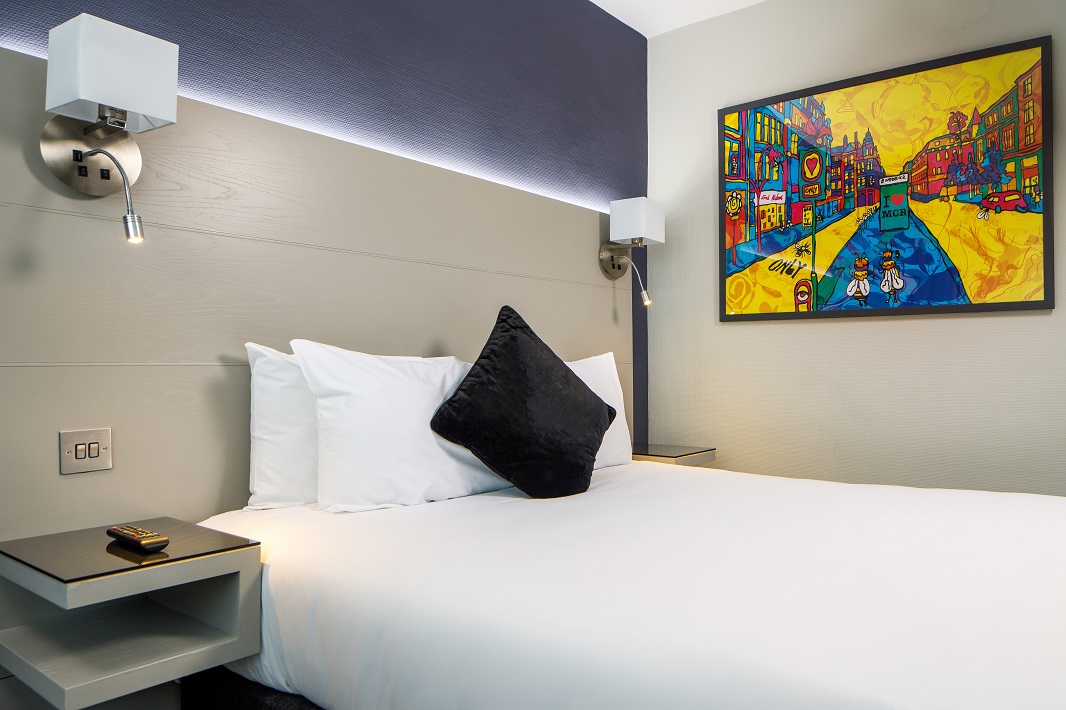 Double Standard Room Web Bedroom with wall art, double bed with lamps and side tables either side of the bed.